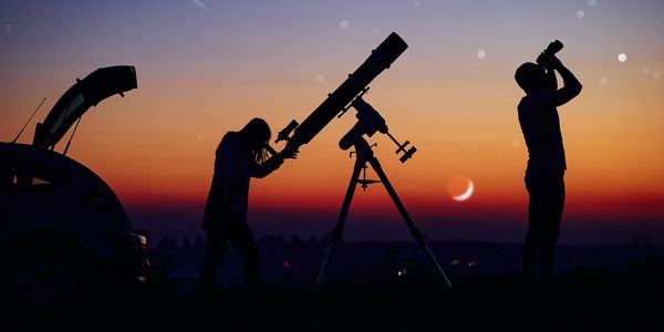 Two people stargazing with a telescope and binoculars at sunset.