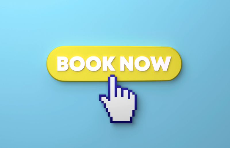 Cursor Hand Clicking Over A Yellow Book Now Push Button On Blue Background. Online booking concept.