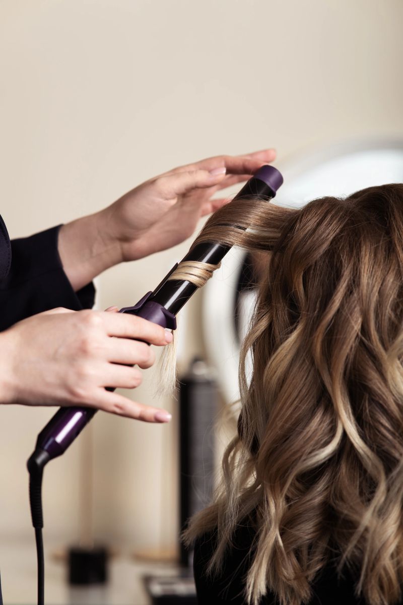 Female hands of a hair master. Close-up of blond hair on a curling iron. Curling curls.