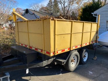 Yellow dump trailer filled with yard debris parked on a driveway.