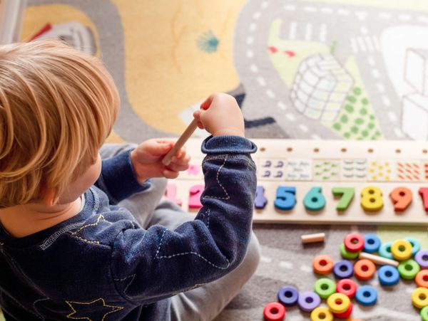 Child playing with colorful number and ring toys on a patterned carpet.