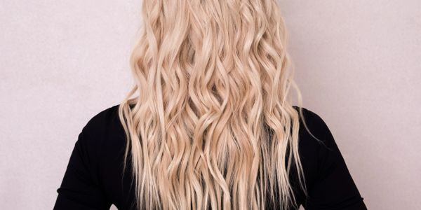 Back view of a person with long, wavy blonde hair and a black top.