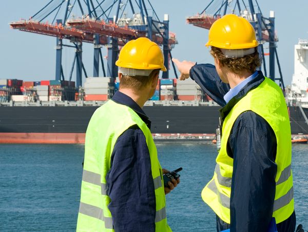 Two dock workers in safety gear inspecting cargo containers at a port.