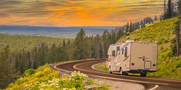 RV driving on a winding road through a scenic forest at sunset.