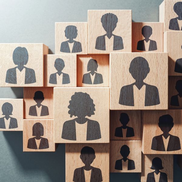Wooden blocks with silhouettes of diverse business people stacked together.