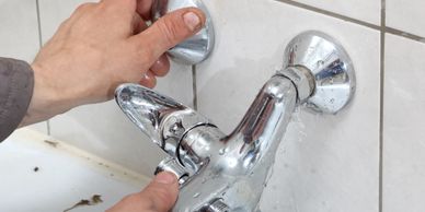 Hands fixing a leaking bathroom faucet with water spraying out.
