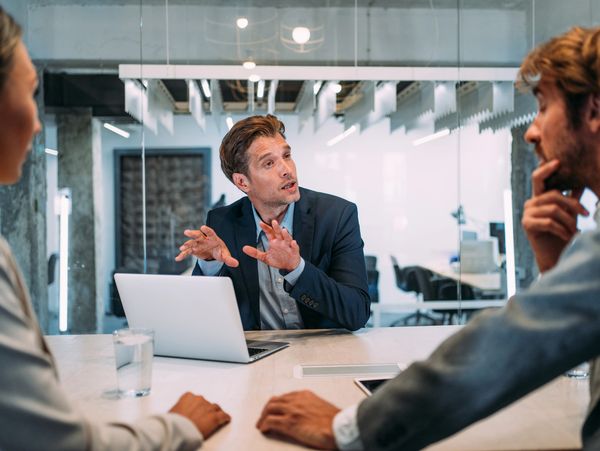 Man explaining something to two colleagues in a meeting room.