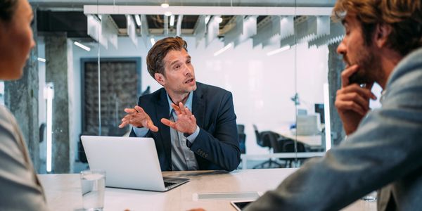Man explaining a concept to colleagues in a modern office meeting.