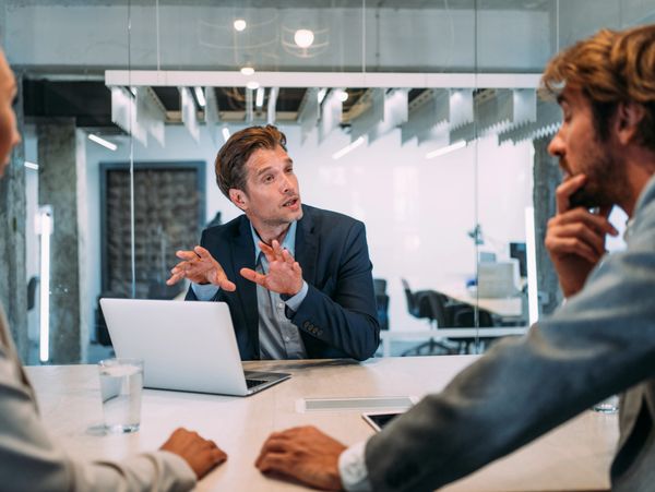Man in blue suit explaining something during a meeting.