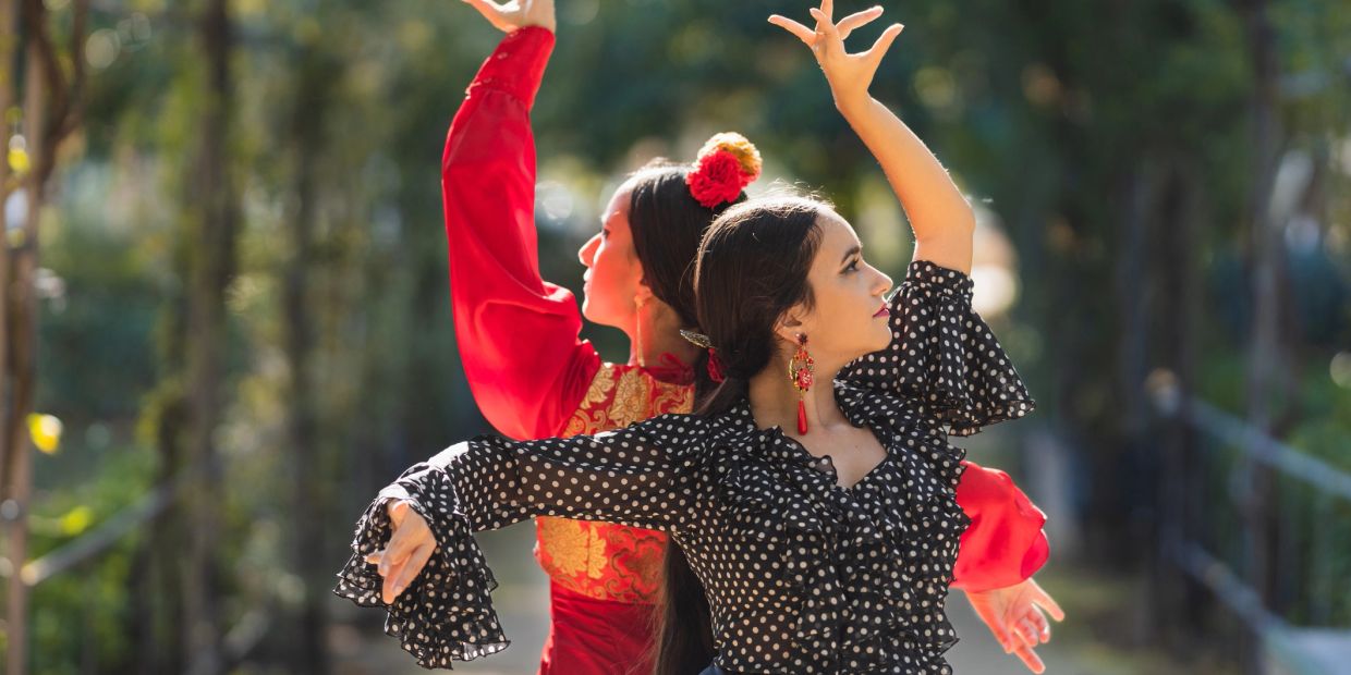 Two women gracefully dancing flamenco outdoors in vibrant attire.