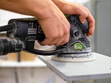 Hands using an electric sander on a wooden board.