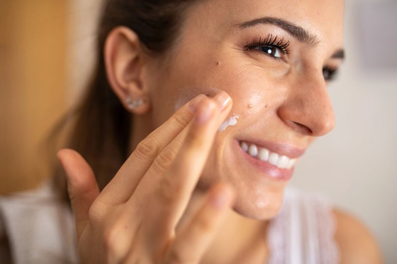 Young woman applying moisturizing cream to her fresh skin