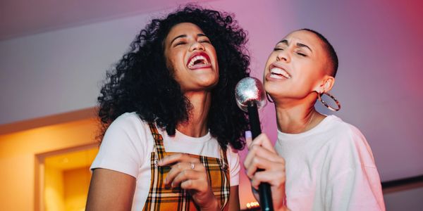 Two women joyfully singing into a microphone together.