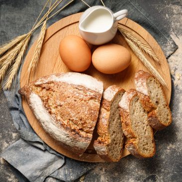 Freshly baked bread, eggs, and a jug of milk on a wooden board.