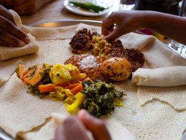Hands enjoying traditional Ethiopian food served on injera bread.
