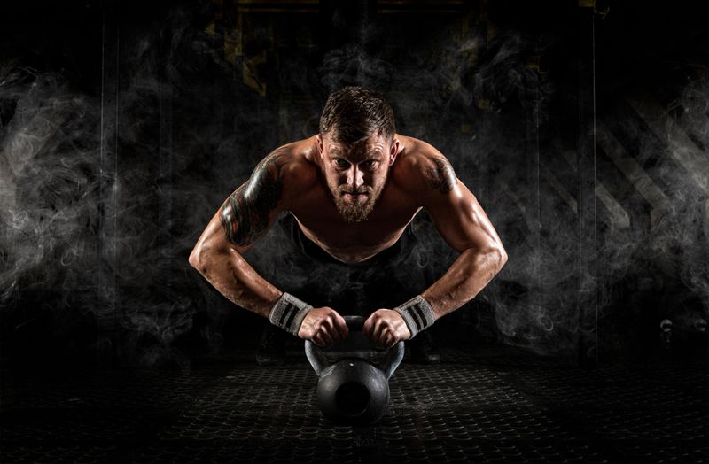 Handsome muscular man doing push ups on kettle ball on dark background