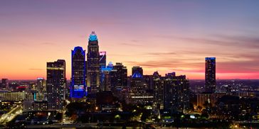 City skyline at sunset with illuminated buildings and a colorful sky.
