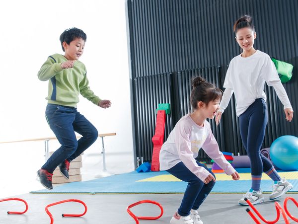 2 children jumping over hurdles with teacher or physical trainer in background watching