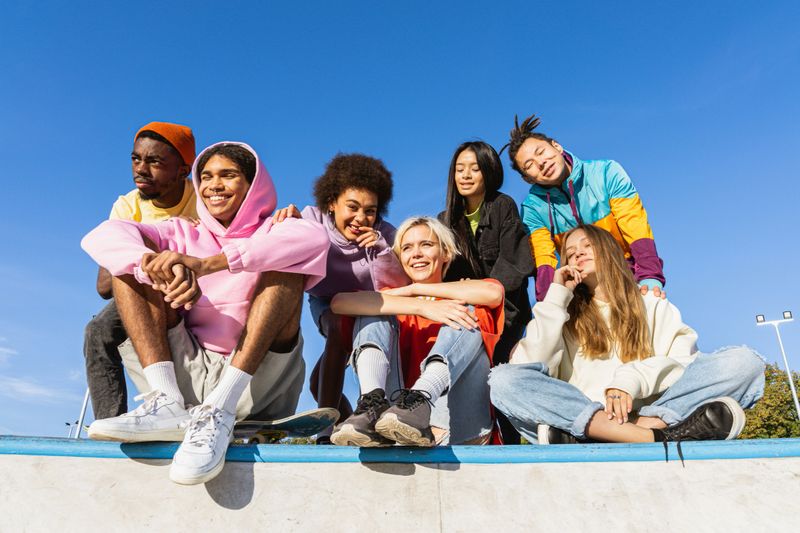 Multicultural group of young friends bonding outdoors and having fun - Stylish cool teens gathering at urban skate park