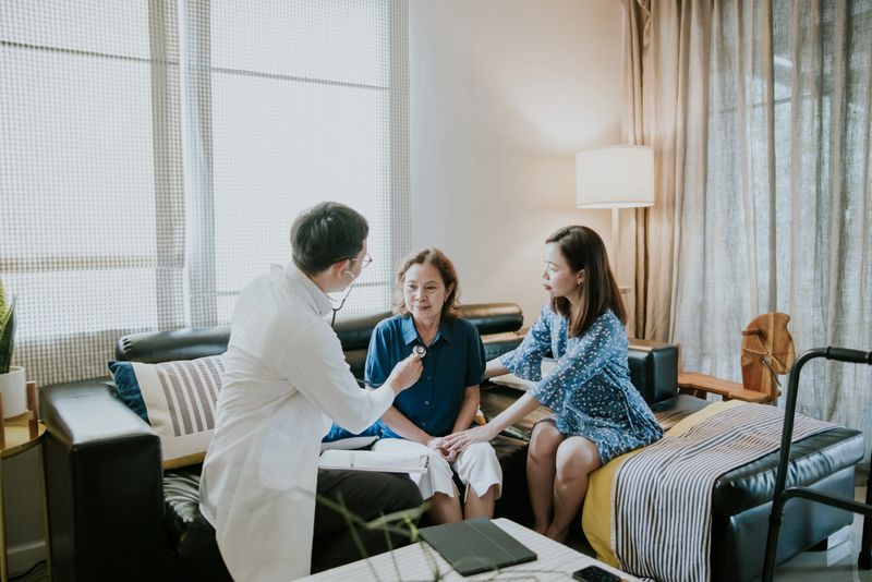 Young Asian male doctor holding stethoscope examining senior grandmother patient for checking heartbeat at homecare checkup medical visit.