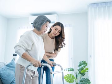 A woman is helping a senior get steady on their feet with their walker.
