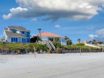 Beach houses with stairs leading to the sandy shore.