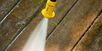 Yellow pressure washer cleaning a wooden deck.