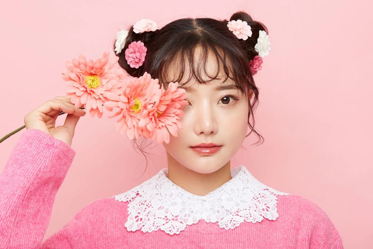 Young woman with flowers in her hair and hand, wearing pink sweater and white lace collar.