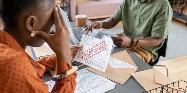 A worried woman holding a past due bill with a man reviewing documents at a table.