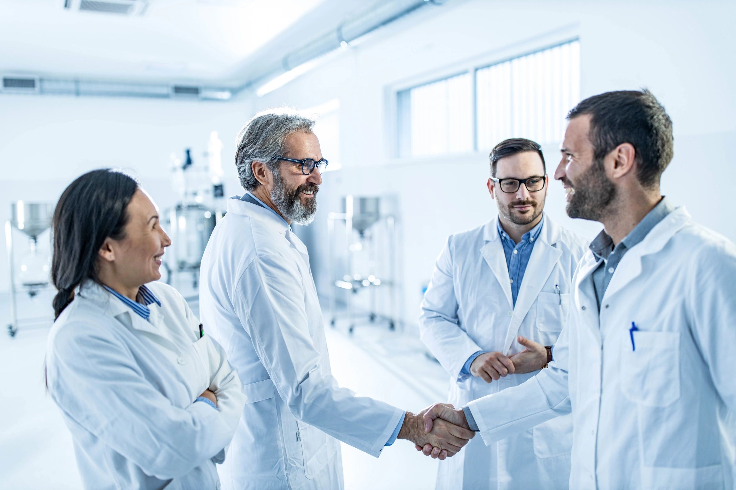 Scientists in lab coats shaking hands in a bright laboratory.