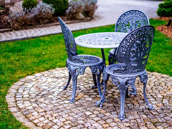 Ornate metal garden table and chairs on cobblestone patio.