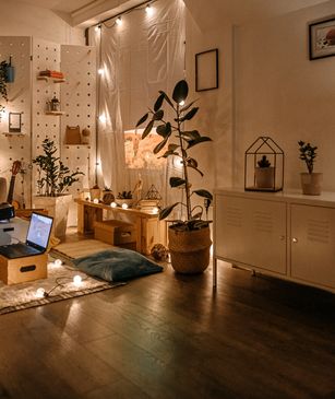 Cozy living room with warm lighting, plants, and a laptop on the floor.