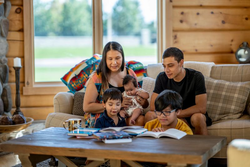 A mother and her kids hang out in their living room, smiling as they take care of the baby of the family.