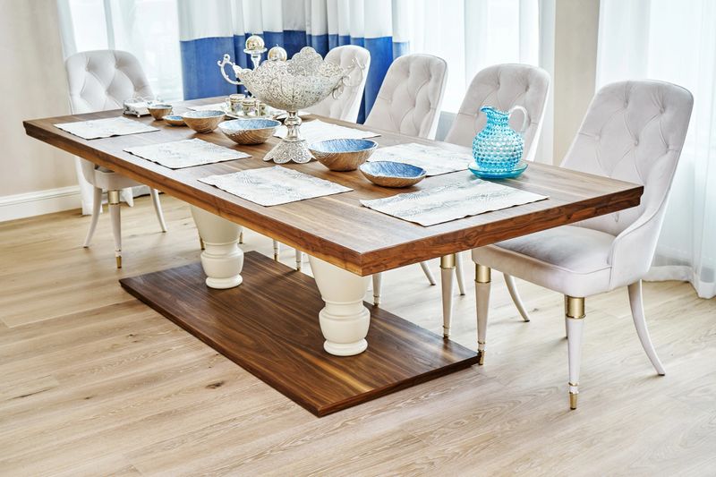 Luxury vintage dining table of walnut solid and veneer wood with festive setting and armchairs near window in spacious room