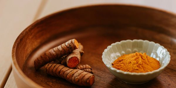 Turmeric root and powder in a wooden bowl on a light surface.