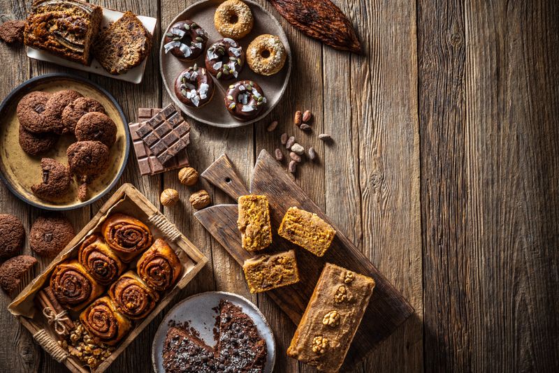 Vegan desserts bakery assortment recipes with all vegan brownie, cinnamon buns, carrot cake, banana cake, donuts and cookies on wooden background