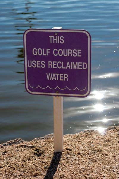 Sign indicating golf course uses reclaimed water by a water body.