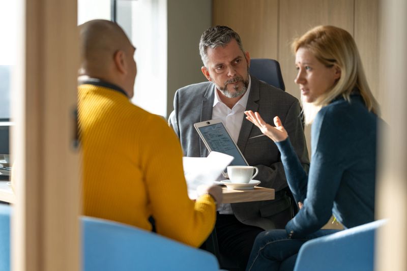 Rear view of a mid adult couple sitting in a financial advisor's office talking about their investment plans while the advisor is listening.