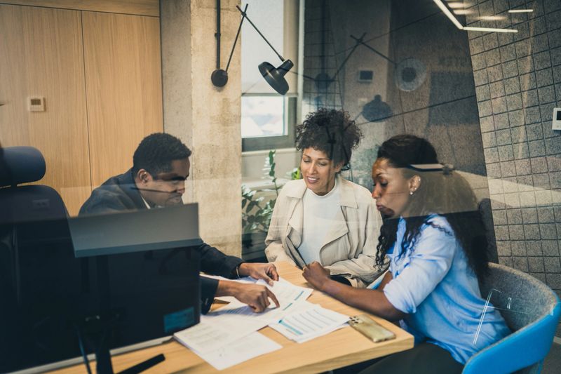African-American financial advisor talking to female couple about investment opportunities.