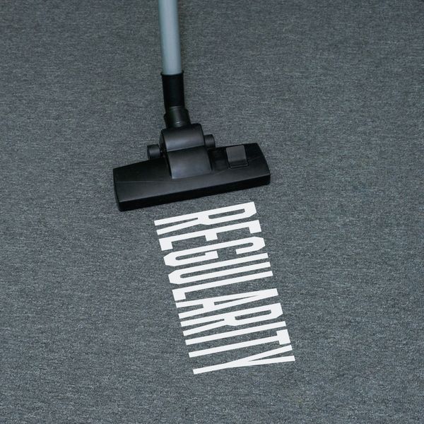 A vacuum cleaner head on carpet with the word 'REGULARITY' appearing cleaned.