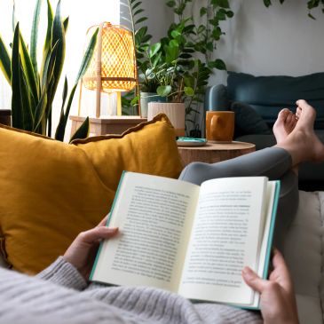 Person reading a book on a cozy couch.