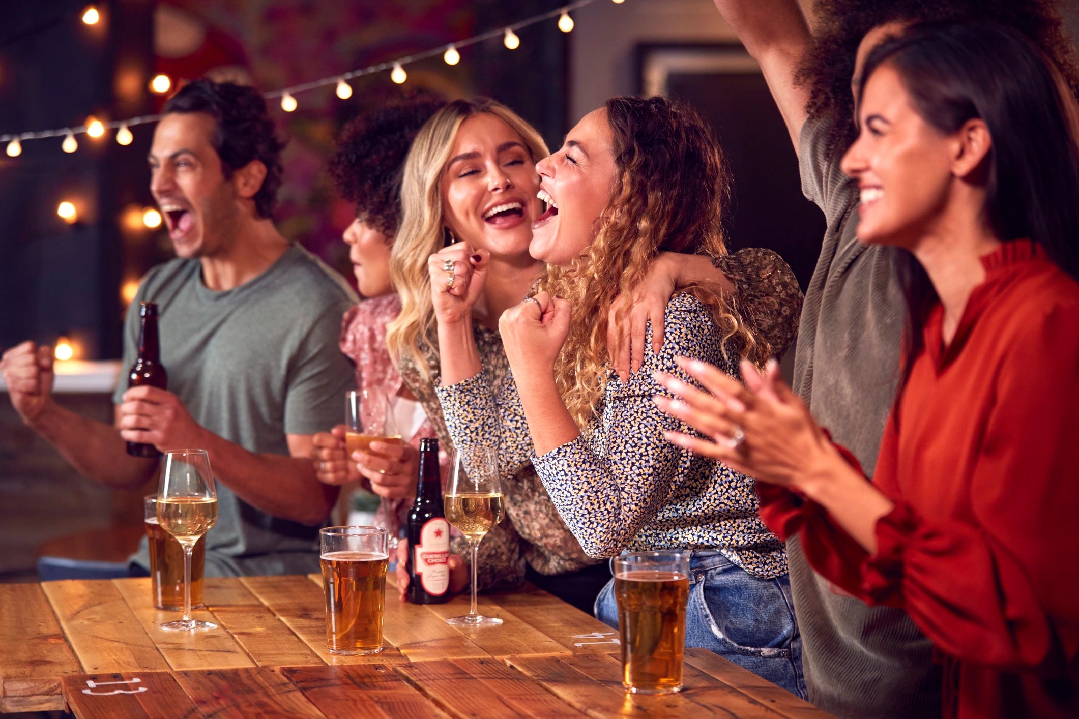 Friends celebrating with drinks and cheering at a party.