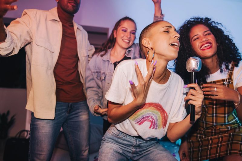 Young woman singing her heart out on karaoke night. Vibrant young woman entertaining her friends with a microphone at a house party. Group of happy young people having a good time on the weekend.
