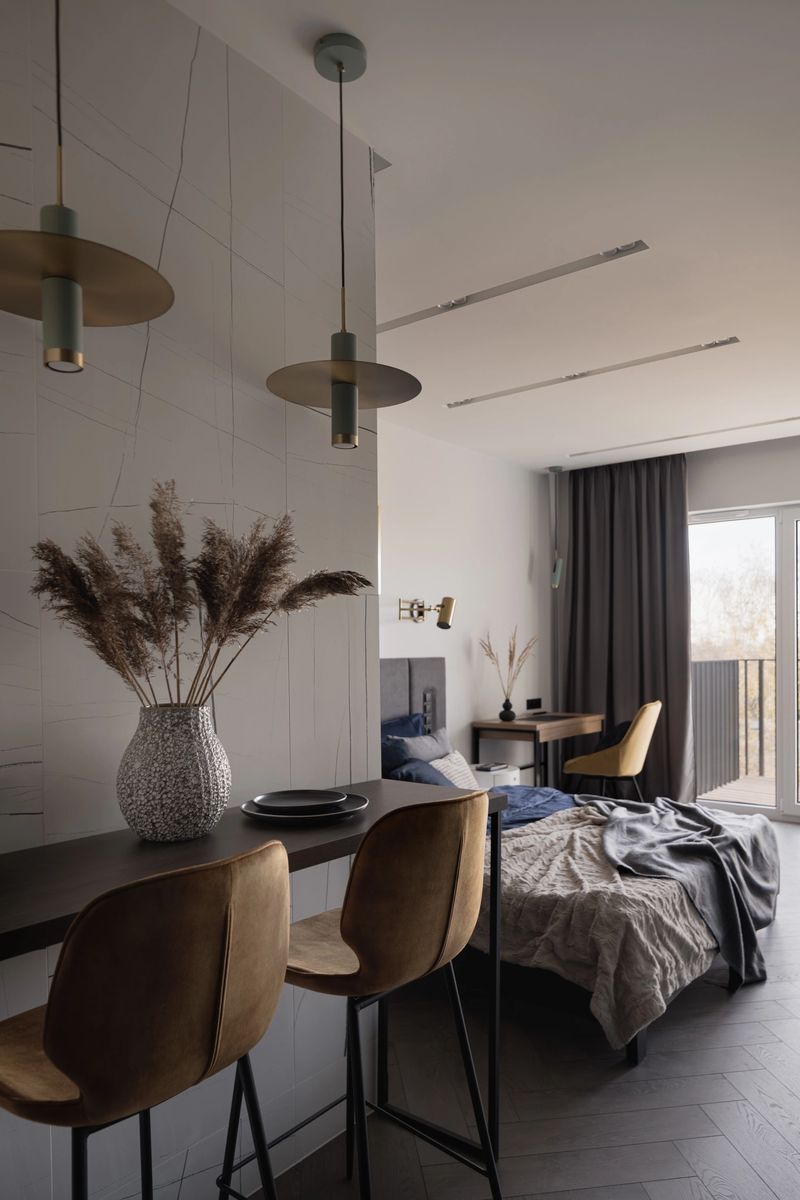 Stylish table with two yellow chairs under two decorative lamps next to bedroom