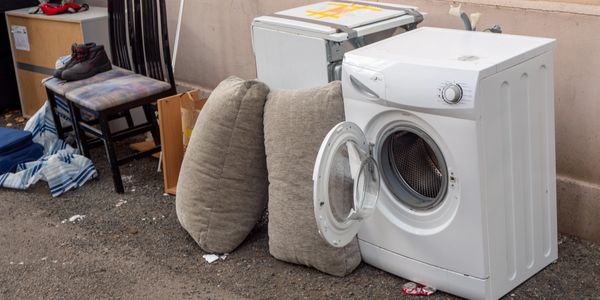 Discarded household items including a washing machine and cushions on the street.