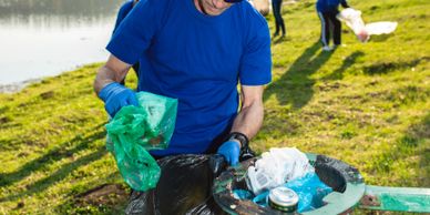 Volunteer cleaning up trash near a water body on a sunny day.