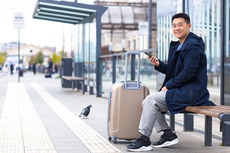 Tourist at the bus station, orders a taxi using the application on the phone, Asian book accommodation online for business travel