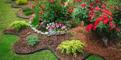 A colorful flower garden with roses, petunias, and decorative edging.