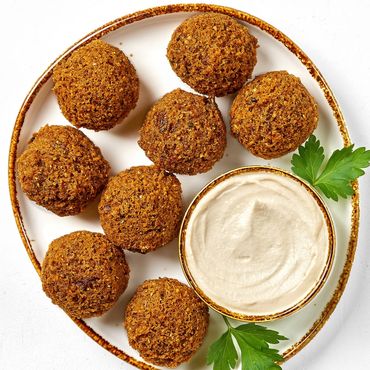 Plate of crispy falafel balls with a bowl of creamy tahini sauce and parsley garnish.