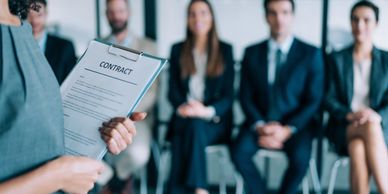 Person holding a contract with a group of professionals seated in the background.
